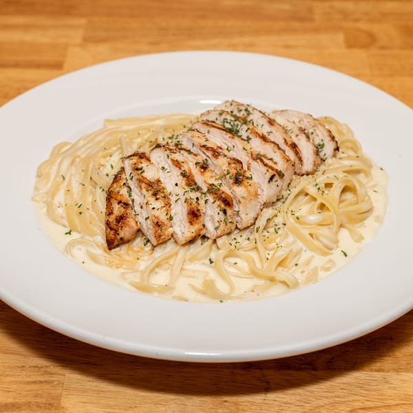 Grilled chicken Alfredo pasta with parsley on a white plate from Papa V's Pizzeria.