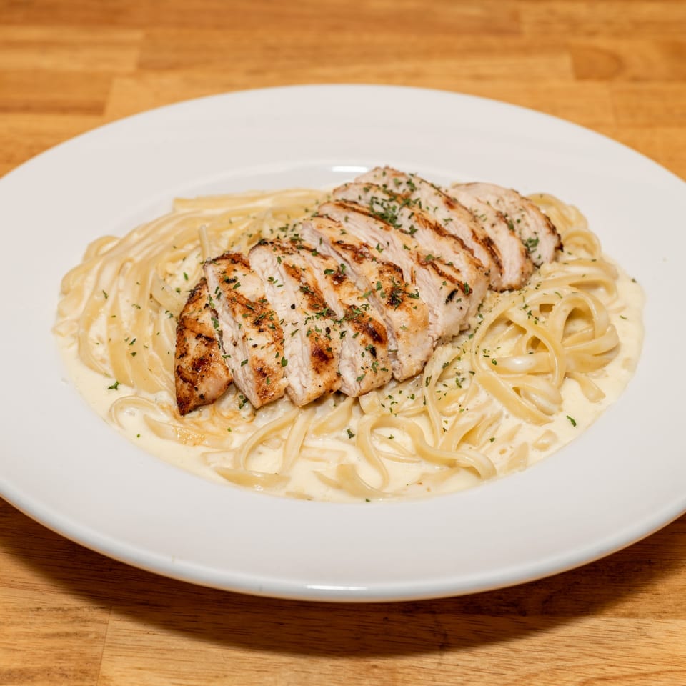 Grilled chicken Alfredo pasta with parsley on a white plate from Papa V's Pizzeria.