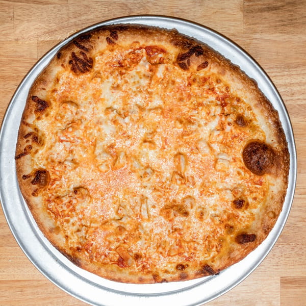 A whole, round Papa V's Pizzeria buffalo chicken pizza on a metal pan, on a wooden table.