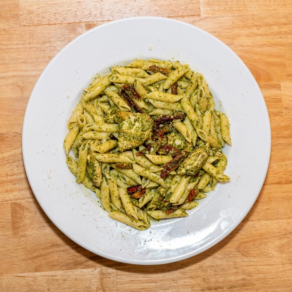 Penne pasta with pesto sauce, chicken, and sun-dried tomatoes on a white plate.