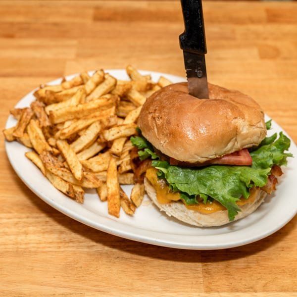 A knife-pierced burger with lettuce, tomato, and cheese, served with a side of fries.