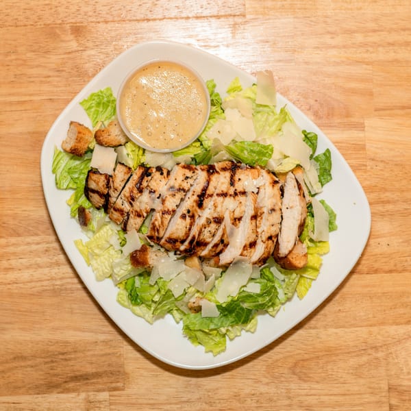Grilled chicken Caesar salad with croutons, parmesan, and dressing on a white plate.