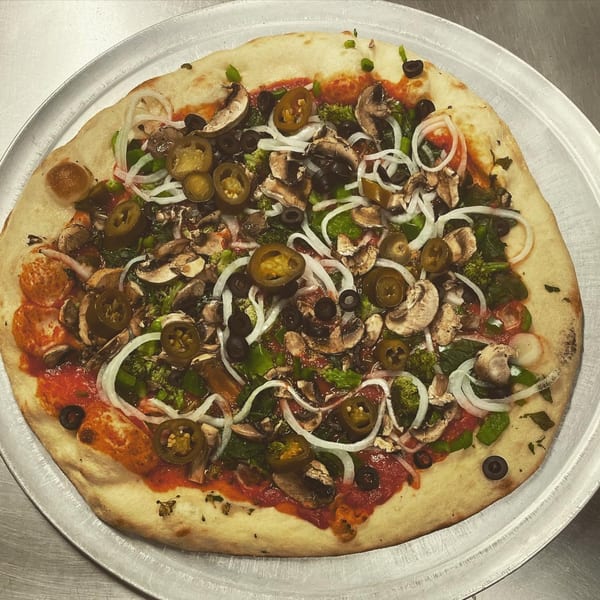 A Papa V's Pizzeria pizza with mushrooms, onions, jalapeños, olives, and broccoli on a metal tray.
