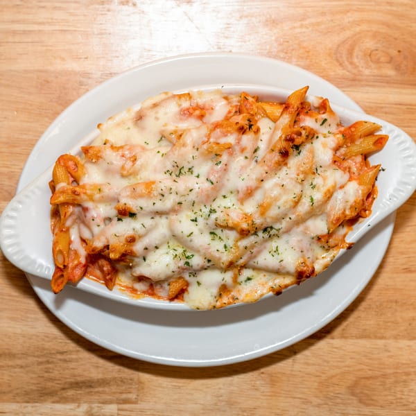 Baked penne pasta with melted cheese and parsley in a white dish on a wooden table.